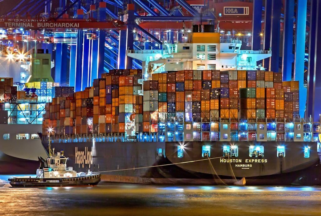 Crafting Captivating Headlines: Your awesome post title goes here A brightly lit cargo ship at Hamburg harbor with stacked containers and a tugboat.